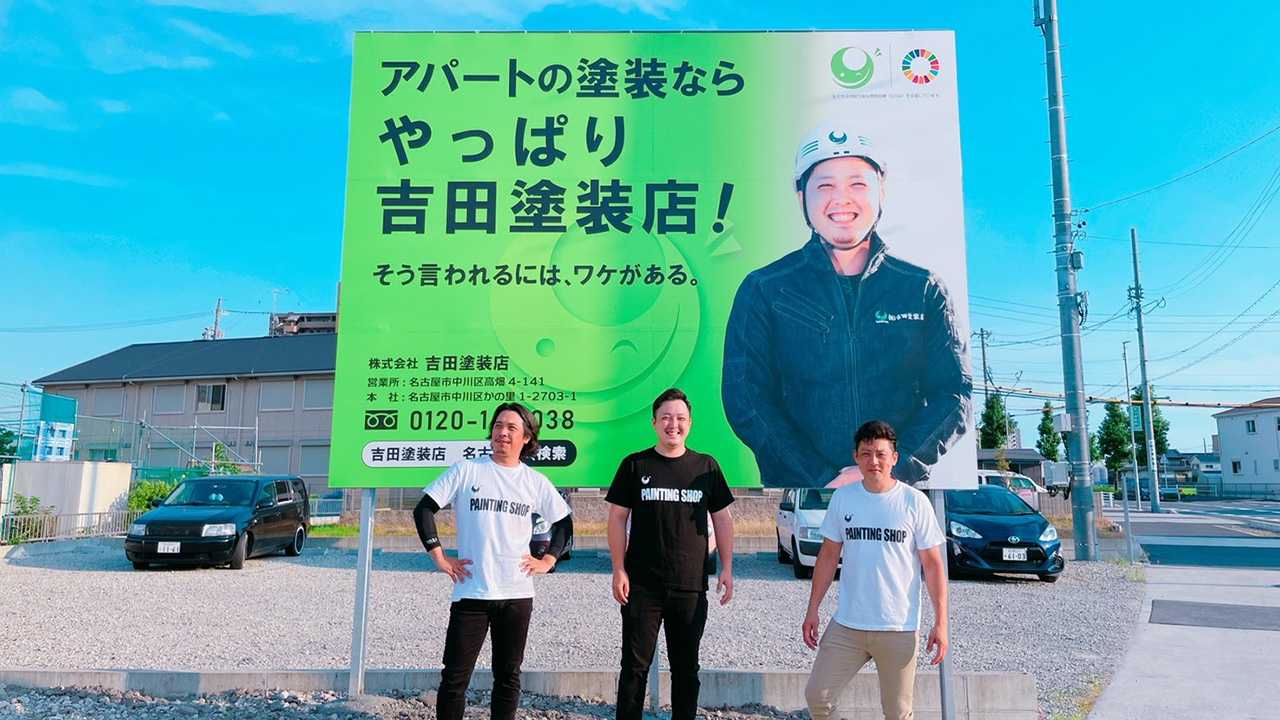 吉田塗装店の看板前に立つ3人の社員