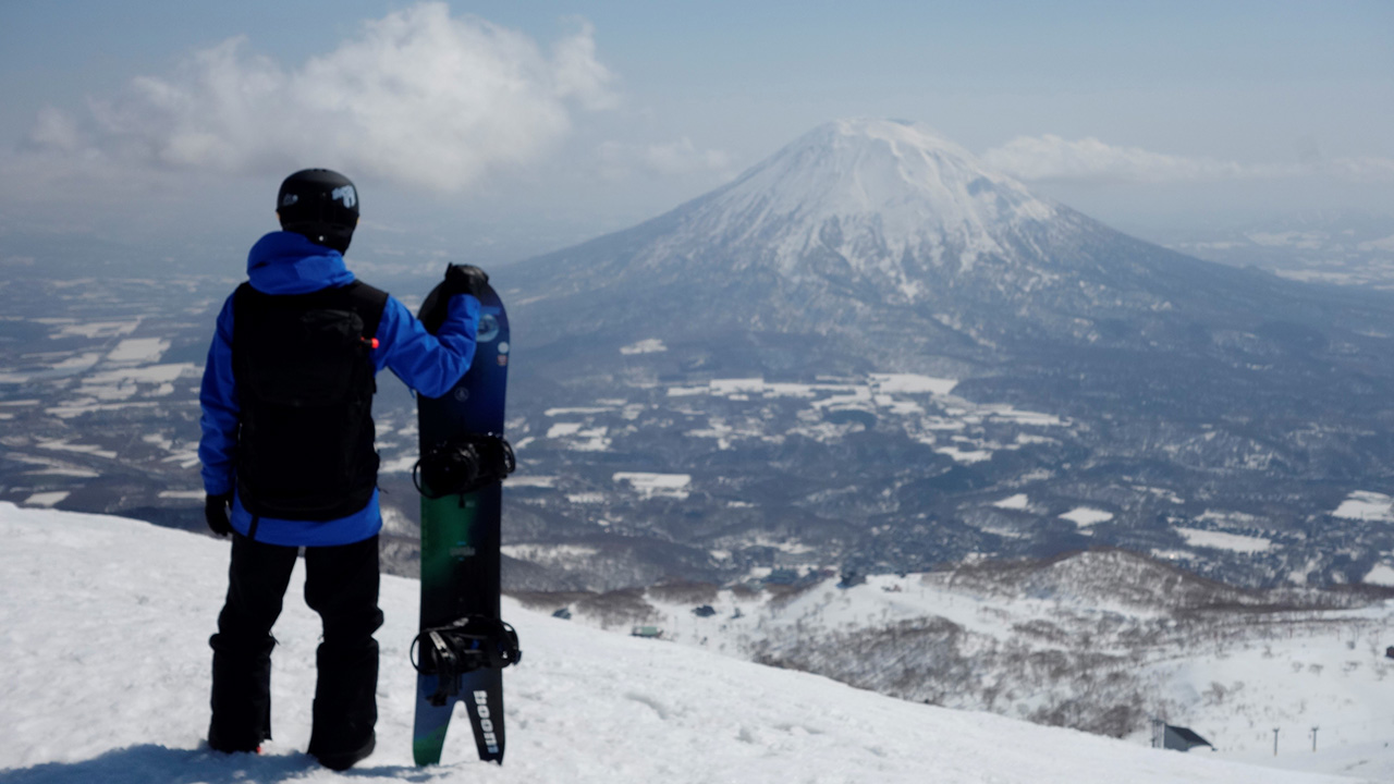 雪をかぶった山景色とスノーボードを持った男性